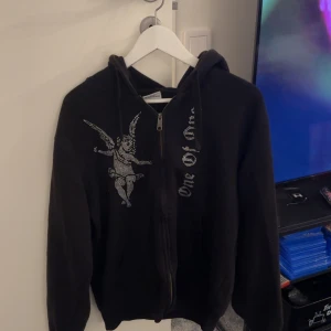 One of one  - Säljer en svart One of one  hoodie med dragkedja. Perfekt för en avslappnad stil. Den har en klassisk passform med långa ärmar och en bekväm huva.