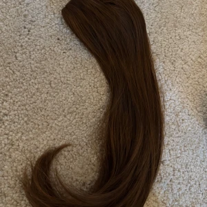 Brun hårförlängning med clips - Säljer en brun hårförlängning med fäste som en klämma. Perfekt för att snabbt få längre och fylligare hår. Enkel att fästa och ta av. Passar bra för både vardag och speciella tillfällen.