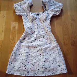 Blommig klänning med puffärmar - Charmig kortklänning med blommigt mönster i ljusa toner. Klänningen har puffiga kortärmar och en smickrande passform. Perfekt för sommarens tillställningar.