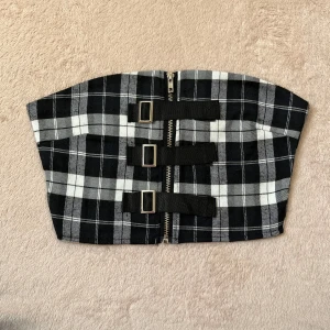 Svart och vit rutig tubtopp - Trendig svart och vit rutig tubtopp med dragkedja och spännen framtill. Endast testad, strl XS.