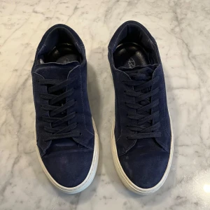 Mörkblå sneakers i mocka och skinn - Snygga mörkblå sneakers i mocka och skinn med vit sula och klassisk snörning. Perfekta för en avslappnad stil.