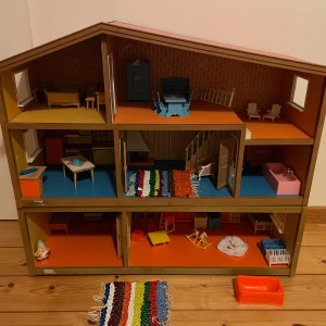 Lundby  dockhus med källare och möbler - Säljer ett charmigt dockhus med tre våningar och detaljerade rum. Inkluderar möbler som sängar, bord, stolar och köksinredning. Perfekt för lek och inredning. Dockhuset har en färgglad matta och en mysig atmosfär.