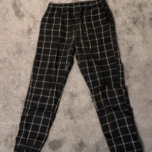 Pyjamas byxor  - Snygga svart/vitt pyjamas byxor med vitt rutmönster och bekväm snörning i midjan. Perfekta för en avslappnad stil med elastisk midja för extra komfort.