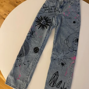 Jeans med konstnärligt tryck från Bershka - Unika jeans från Bershka med ett konstnärligt tryck i svart och rosa. De har en straight passform och är tillverkade i denim. Perfekta för dig som vill sticka ut med en kreativ stil.