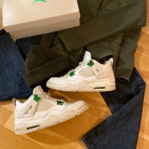 Jordan 4 metallic green - Snygga Nike Air Jordans i vitt med gröna detaljer. Skorna har en klassisk design med snörning och den ikoniska Jumpman-loggan. Perfekta för dig som vill ha en stilren look med en touch av färg. Låda finns