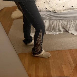 Svarta jeans med leoparddetaljer - Unika svarta jeans med leopardmönstrade detaljer längs sidorna och på bakfickan. Perfekt för dig som vill sticka ut med en djärv stil. Jeansen har en klassisk passform och är tillverkade i ett slitstarkt material.
