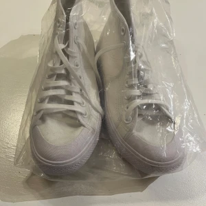 Adidas sneakers med snörning - Snygga vita sneakers med hög modell och klassisk snörning. Skorna har en robust sula med bra grepp och är perfekta för en stilren look. Tillverkade i ett slitstarkt material som ger en fräsch känsla. Helt nya aldrig använda 