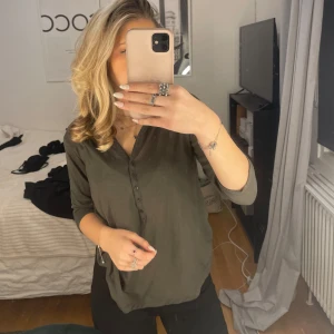 Olivgrön blus med knappar - Säljer en stilren olivgrön blus med knappar framtill. Blusen har trekvartsärmar och en v-ringad design. Perfekt för en avslappnad men ändå elegant look.🤍💗