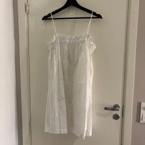 Vit axelbandslös klänning - Säljer en luftig vit klänning med smala axelband och elastisk överdel. Perfekt för varma sommardagar. Klänningen har en avslappnad passform och är tillverkad i ett lätt material.