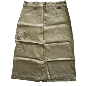 Olivgrön kjol med fickdetalj - Snygg olivgrön kjol med praktisk ficka på sidan och dragkedja baktill. Kjolen har en klassisk design med knappar i midjan och en bekväm passform. Perfekt för en stilren look!