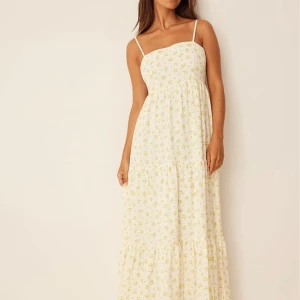 Blommig långklänning från NAKD x Lisa&Lena - Charmig långklänning från Lisa & Lena för NA-KD i en ljus färg med sött blommönster. Klänningen har smala axelband och en luftig passform, perfekt för varma dagar. 