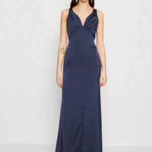 Mörkblå långklänning med v-ringning - Elegant mörkblå långklänning med djup v-ringning och breda axelband. Klänningen har en figurnära passform och är perfekt för festliga tillfällen. Materialet ger en fin glans och faller vackert längs kroppen. Har aldrig använt, har endast provat några gånger.