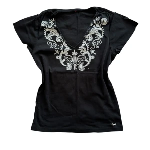 Svart topp med broderade detaljer - Stilren svart topp från Esprit med vacker broderad design kring V-ringningen. Mjukt och skönt material, perfekt för både vardag och festliga tillfällen. Sitter som M.