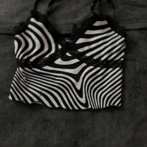 Zebramönstrad ribbad topp - Säljer en cool zebramönstrad ribbad topp med spetsdetaljer. Toppen har smala axelband och en v-ringad design. Perfekt för att ge en edgy touch till din outfit(priset sänks för hållet men det är knappt märkbart och är lätt att sy ihop)