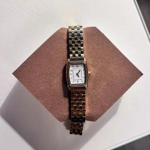 Elegant klocka med rektangulär urtavla - Stilren klocka med rektangulär vit urtavla och en tvåfärgad länk i guld. Klockan har tydliga svarta siffror och visare, vilket ger en klassisk look. Perfekt för den som söker en tidlös accessoar.  Köpt för 1000kr och är inte sliten 