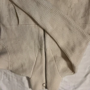 Vit ribbad kofta från Axel Arigato - Säljer en stilren vit ribbad kofta från Axel Arigato. Koftan har en dragkedja framtill och långa ärmar. Perfekt för en avslappnad och trendig look. Passar bra till både jeans och kjol.