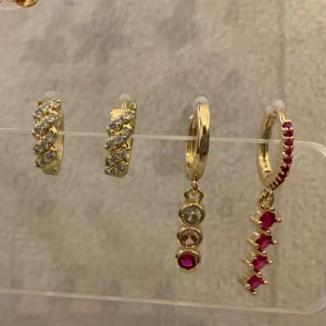 Goldplätarat örhängen  med stenar - Säljer ett set med guldörhängen, inklusive två par med klara stenar och två par med hängande detaljer. Ett par har röda stenar i en rad och det andra har en mix av klara och röda stenar. Perfekt för att mixa och matcha!