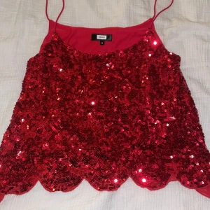 Röd paljettlinne från Bik Bok - Säljer ett glittrande rött linne från Bik Bok, täckt med paljetter och tunna axelband. Perfekt för en festlig kväll! Linnet har en vågig kant nertill som ger en extra touch av stil.