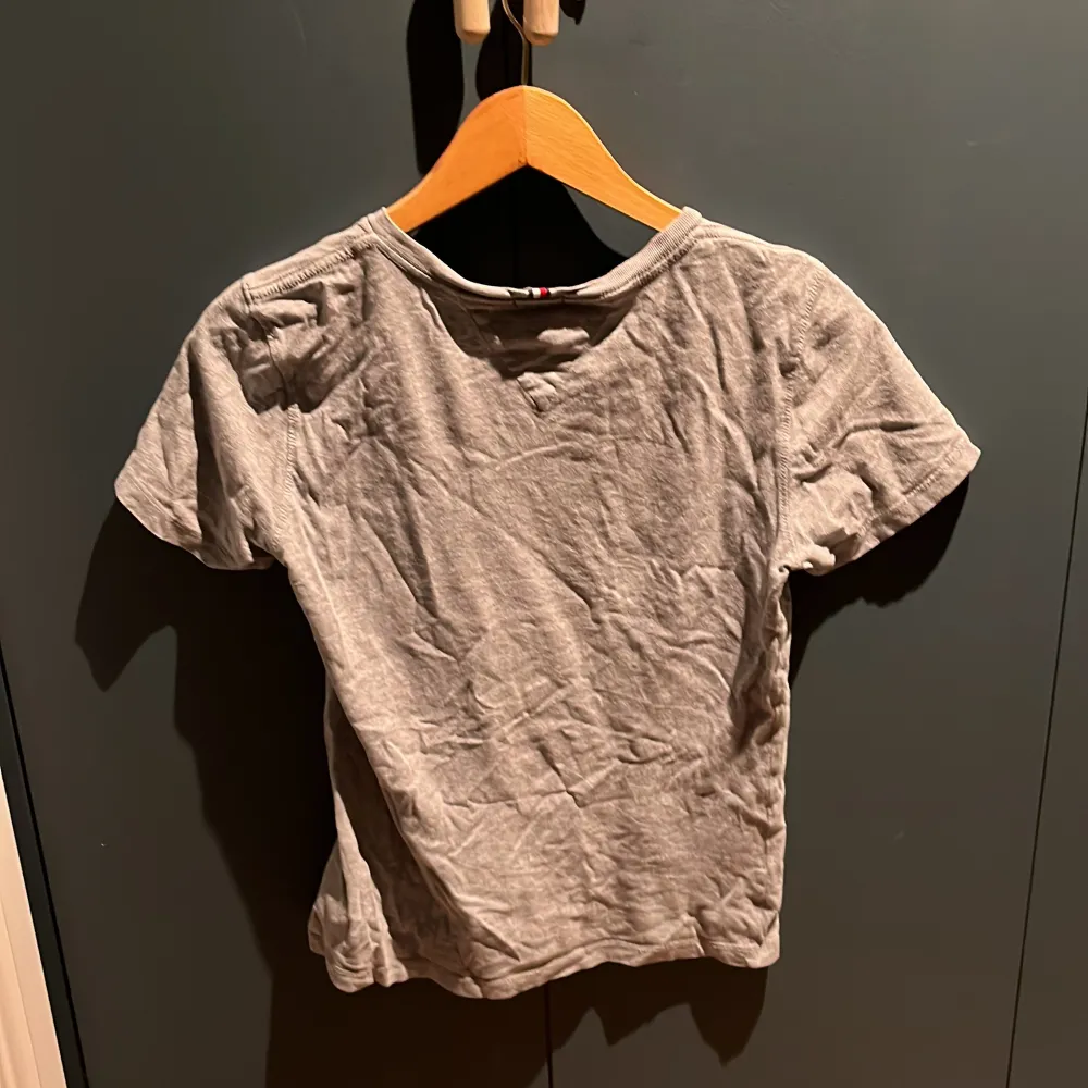 Säljer en grå t-shirt från Tommy Hilfiger i ekologisk bomull. T-shirten har korta ärmar och ett tryck med märkesloggan på framsidan. Lite nöt tryck men ändå väldigt bra skick. T-paidat.