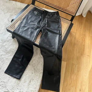 Svarta skinnbyxor - Snygga svarta skinnbyxor med en stilren design. Byxorna har en rak passform och är perfekta för en trendig look. De har en klassisk midja och är tillverkade i ett glansigt skinnmaterial.