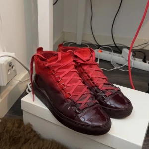 REDD Balenciaga Arena - Snygga röda sneakers från Balenciaga med en glansig finish och snörning. Skorna har en djup röd färg och en robust sula. Perfekta för att ge din outfit en lyxig touch. Storlek 41 men passar 42