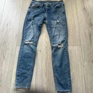 Blå jeans från Calvin Klein - Snygga blå Calvin Klein jeans med skinny fit och midwaist. De har slitna detaljer på knäna och fransiga benslut för en trendig look. Perfekta för en avslappnad stil.
