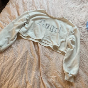 Vit croppad tröja från Shein - Säljer en vit croppad tröja från Shein med texten 'Angel' i glittriga bokstäver på framsidan. Tröjan har långa ärmar och en avslappnad passform. Perfekt för en trendig look! 🌟skulle själv säga att det tar emot att sälja den men har tyvärr växt ur den. 