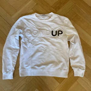 Vit sweatshirt från Dondup - Säljer en stilren vit sweatshirt från Dondup med textdetalj på framsidan. Tröjan har långa ärmar och en klassisk rund halsringning. Perfekt för en avslappnad look.