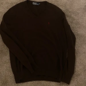 Brun tröja från Polo Ralph Lauren - Säljer en stilren brun tröja från Polo Ralph Lauren med v-ringning och det klassiska logotypbroderiet i röd på bröstet. Tröjan har långa ärmar och är perfekt för en elegant vardagslook. Passar bra till både jeans och chinos.