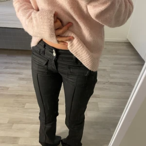 Svarta byxor  - Säljer de populära svarta byxor med låg midja och bootcut-stil från nelly. Byxorna har dekorativa knappar framtill och flera fickor. Perfekta för en stilren look. Lite mer som läder byxor i materialet och nyligen köpta men för små tyvärr