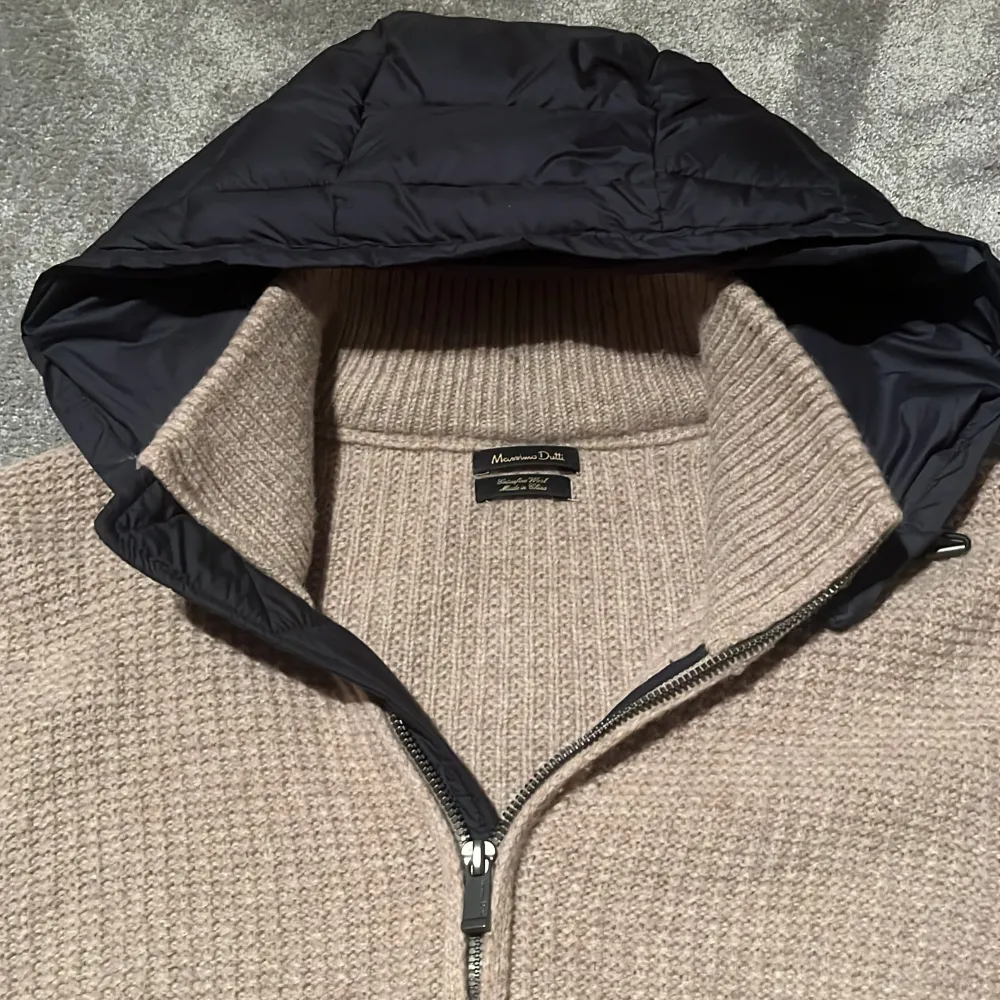 Säljer en snygg beige stickad cardigan från Massimo Dutti. Tröjan har en dragkedja framtill och en quiltad huva i svart. Perfekt för kyliga dagar med sin stilrena design och bekväma passform. Storlek M och passar runt 180! INGA BYTEN!. Neuletakit & Villapaidat.