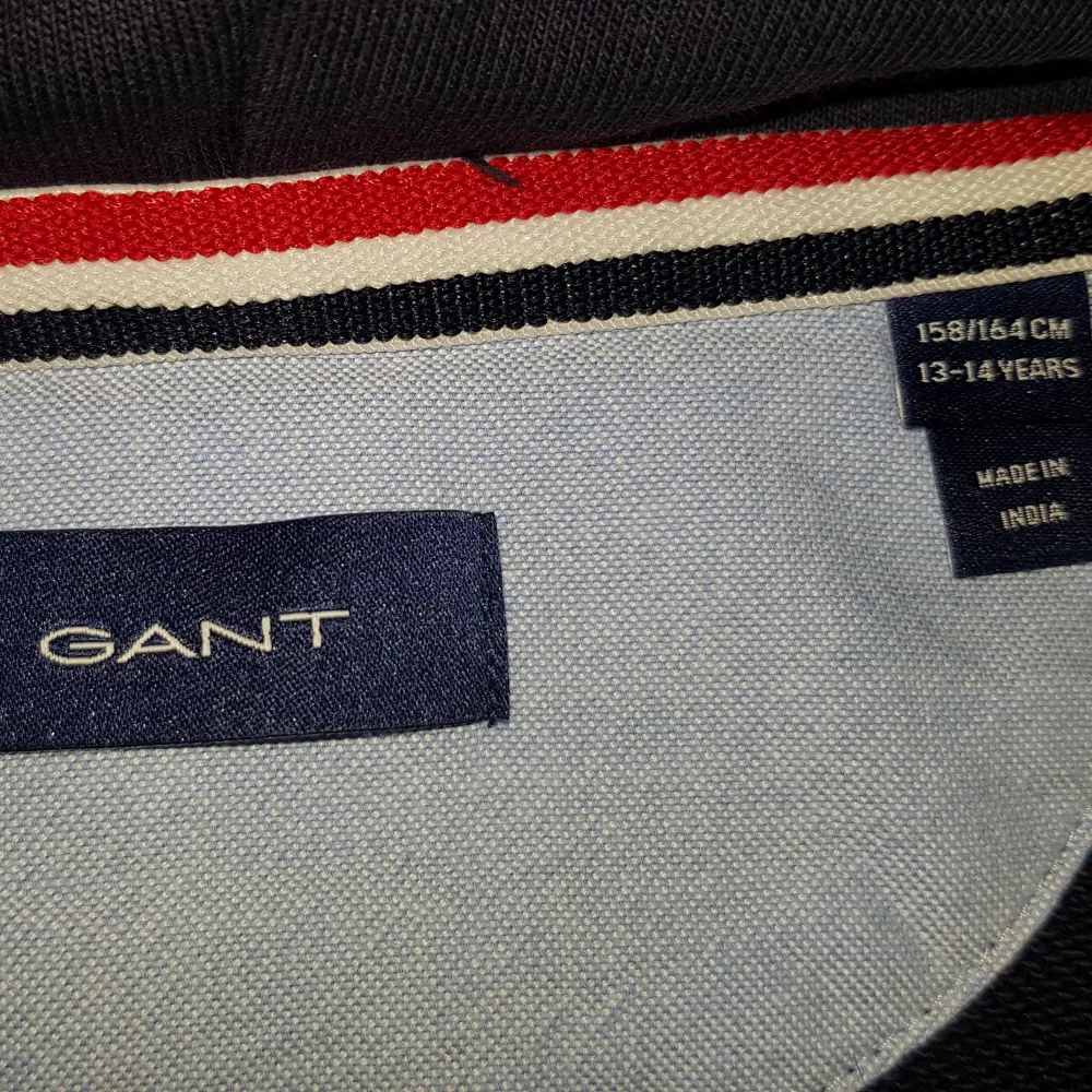 Säljer en marinblå hoodie från GANT med broderad logga på bröstet. Den har en klassisk design med luva och en stor ficka framtill. Snygg tröja för en avslappnad look. Mjukt sweatshirt-material i 98% bomull, 2% elastan. Storlek 158-164.. Hupparit & Collegepaidat.