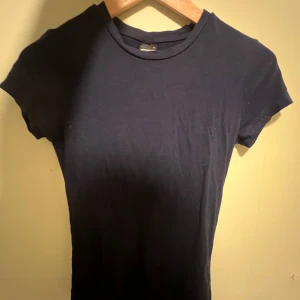 Mörkblå  t-shirt från Gina Tricot - Säljer en klassisk mörkblå  t-shirt från Gina Tricot. Den har en rund halsringning och korta ärmar, perfekt för en enkel och stilren look. Passar till det mesta och är ett måste i garderoben.