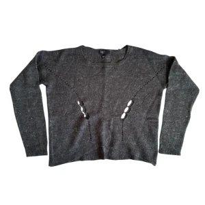 Grå stickad tröja - Säljer en grå stickad tröja med unikt hålmönster framtill. Tröjan har långa ärmar och en rund halsringning. Perfekt för en stilren och bekväm look.