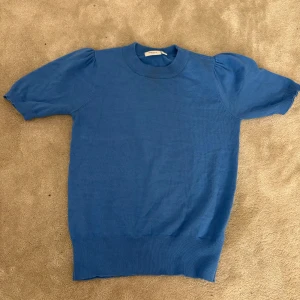 Blå kortärmad tröja - Säljer en snygg blå tröja med korta ärmar och ribbad nederkant.