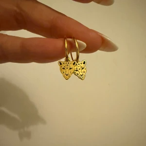 Guldörhängen med leopardmotiv - Snygga guldörhängen med leopardmotiv. Dessa örhängen har en rund form med ett hängande leopardhuvud i guld. Perfekta för att ge en djärv touch till din stil.