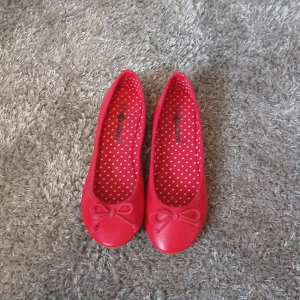 Röda ballerinaskor med rosett - Snygga röda ballerinaskor från Bullhead med en söt rosett på tån. Insidan har ett prickigt mönster i vitt och rött. Perfekta för en färgglad touch till din outfit.
