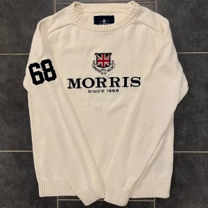 Vit tröja från Morris - Säljer en stilren vit tröja från Morris med svart text och en Union Jack-logga på bröstet. Tröjan har nummer 68 tryckt på ärmen och är tillverkad i 100% bomull. Perfekt för en avslappnad och snygg look.