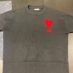 Ami paris tröja  - Säljer en stilren svart tröja från Ami Alexandre Mattiussi med ett rött hjärta och bokstaven A broderat på bröstet. Tröjan har en ribbad nederkant och ärmar, vilket ger en snygg passform. Perfekt för en trendig look!