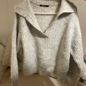 Grå stickad tröja från Gina Tricot - Säljer en mysig grå stickad tröja från Gina Tricot. Tröjan har en bred krage och långa ärmar, perfekt för kyliga dagar. Den är i en stilren grå färg som passar till det mesta. Perfekt för höst och vinter!