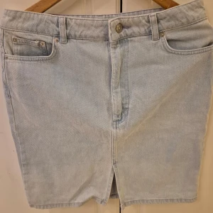 Ljusblå jeanskjol från NA-KD - Snygg ljusblå jeanskjol från NA-KD med klassisk femficksdesign och knappgylf. Perfekt för en avslappnad stil. Kjolen har en kort längd och är tillverkad i ett bekvämt denimtyg.