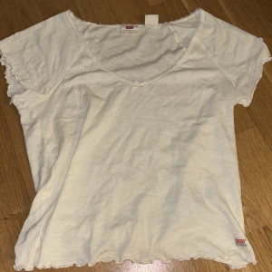 Vit t-shirt från Levi's - Säljer en vit t-shirt från Levi's med u-ringning och korta ärmar. T-shirten har en enkel design med vågiga kanter vid ärmslut och nederkant. Skriv om du vill ha fler bilder💞💞
