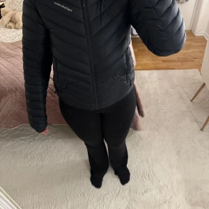 Svart dunjacka från Peak Performance - Säljer en svart dunjacka från Peak Performance. Jackan har en dragkedja framtill och en huva för extra värme. Den är perfekt för kyligare dagar och har en stilren design med diskret logga på ärmen.