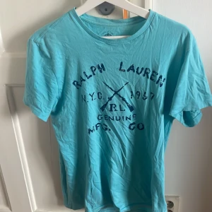 Turkos t-shirt från Ralph Lauren - Säljer en turkos t-shirt från Ralph Lauren med tryck på framsidan. T-shirten är kortärmad och tillverkad i bomull, perfekt för en avslappnad stil. Märket är Polo Jeans Co. och storleken är small.