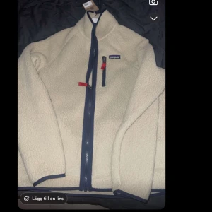 Beige fleecejacka från Patagonia - Säljer en beige fleecejacka från Patagonia med mörkblå dragkedja och detaljer. Jackan har en bröstficka med dragkedja och lite röda detaljer. Sprillans ny med prislapp. Köpt för 1600 men säljer vid bäst prisförslag, jackan är i storlek M. Bara att höra av sig vid frågor osv.