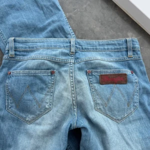 Blå jeans från Wrangler - Snygga blå jeans från Wrangler med broderade bakfickor. De har en bootcut-stil.  Jag är 166 cm och de går ända ner till golvet. Midjemått: 41 cm Innerbenslängd: 78 cm💗