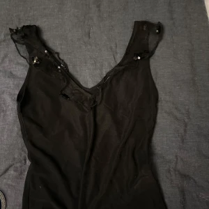 Svart ärmlös topp från Bik Bok - Säljer en svart ärmlös topp från Bik Bok i storlek XS. Toppen har spetsdetaljer och små paljetter vid axlarna som ger en elegant touch. Perfekt för en kväll ute eller en speciell tillställning.