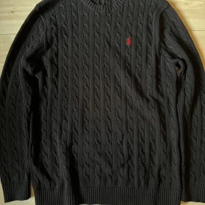 Svart kabelstickad tröja från Ralph Lauren - Säljer en stilren svart kabelstickad tröja från Ralph Lauren med det klassiska röda logotypen på bröstet. Priset kan diskuteras vid snabb affär.
