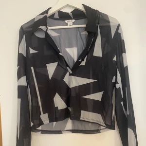Svart och vit mönstrad blus från Monki - Mesh blus från Monki i svart och vitt geometriskt mönster. Blusen har långa ärmar. 