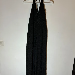 Svart långklänning från Bik Bok - Elegant svart långklänning från Bik Bok med v-ringad hals och knytband i nacken. Klänningen har ett subtilt blommigt mönster som ger en lyxig känsla. Perfekt för speciella tillfällen.🥰🥰🥰